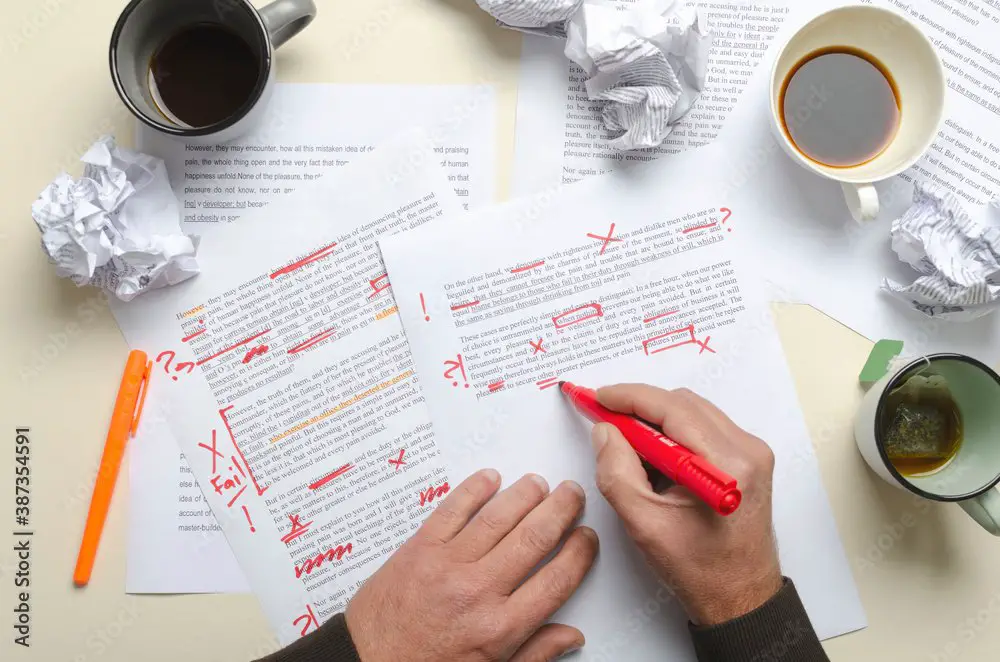 Top view of cups of coffee, crumpled paper, documents and red marks on it.Man proofreading story and has lot of work