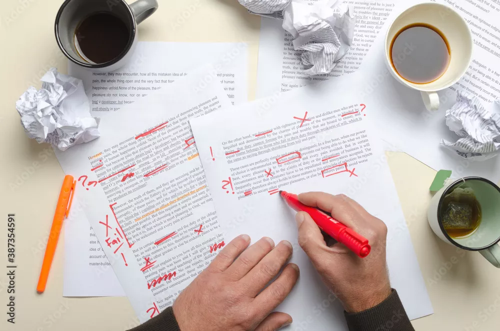 Top view of cups of coffee, crumpled paper, documents and red marks on it.Man proofreading story and has lot of work